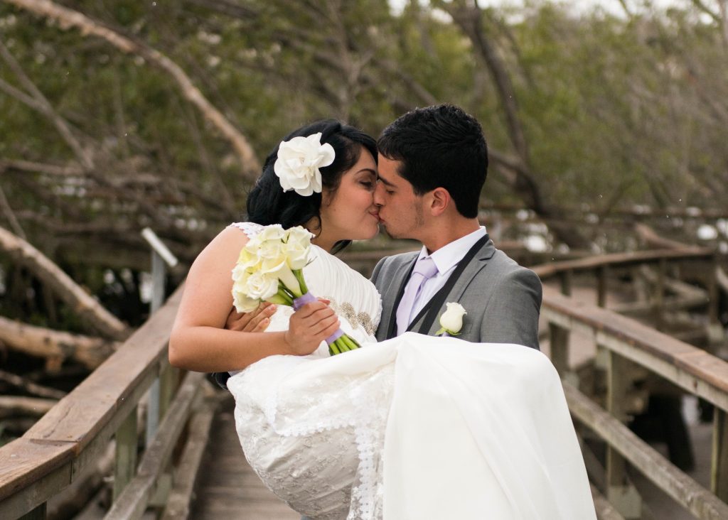 The couple kiss as the groom carries the bride on the boardwalk.